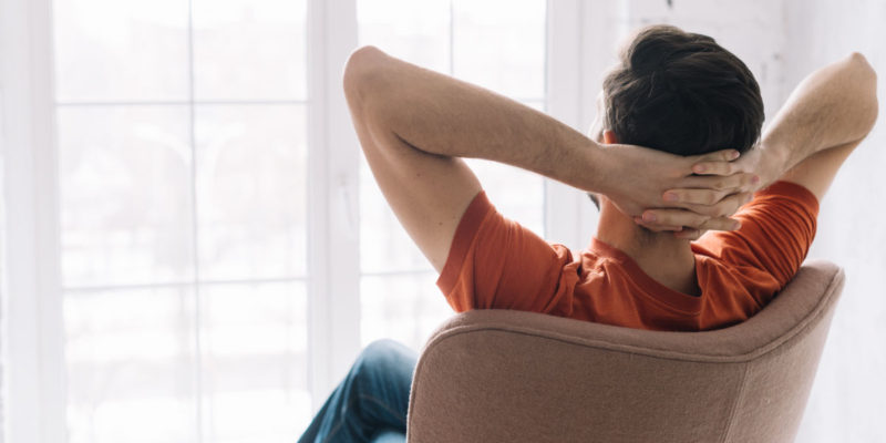 foto de homem sentado em uma cadeira com as mãos na nuca em posição de relaxamento de