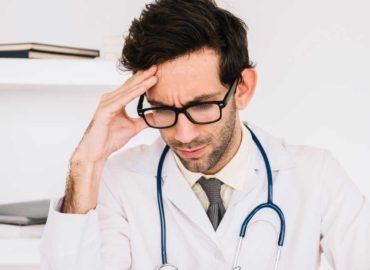 foto de um médico em seu trabalho com a mão direita na cabeça e semblante estressado e preocupado