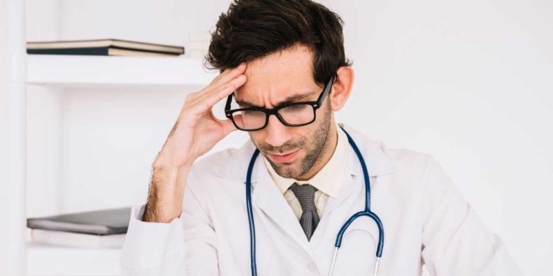 foto de um médico em seu trabalho com a mão direita na cabeça e semblante estressado e preocupado