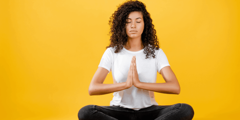 Foto de uma mulher negra meditando em fundo amarelo